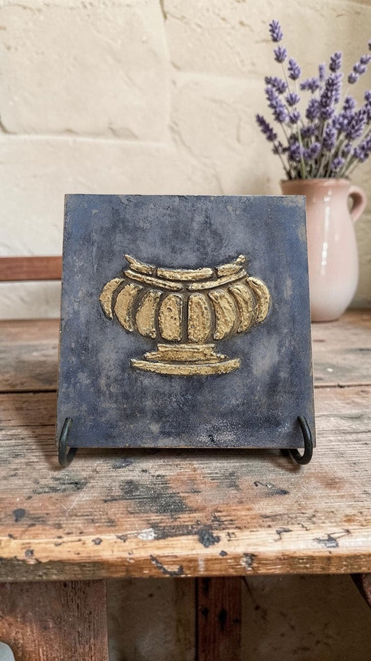 Aged gilded urn wall art displayed on a small easel