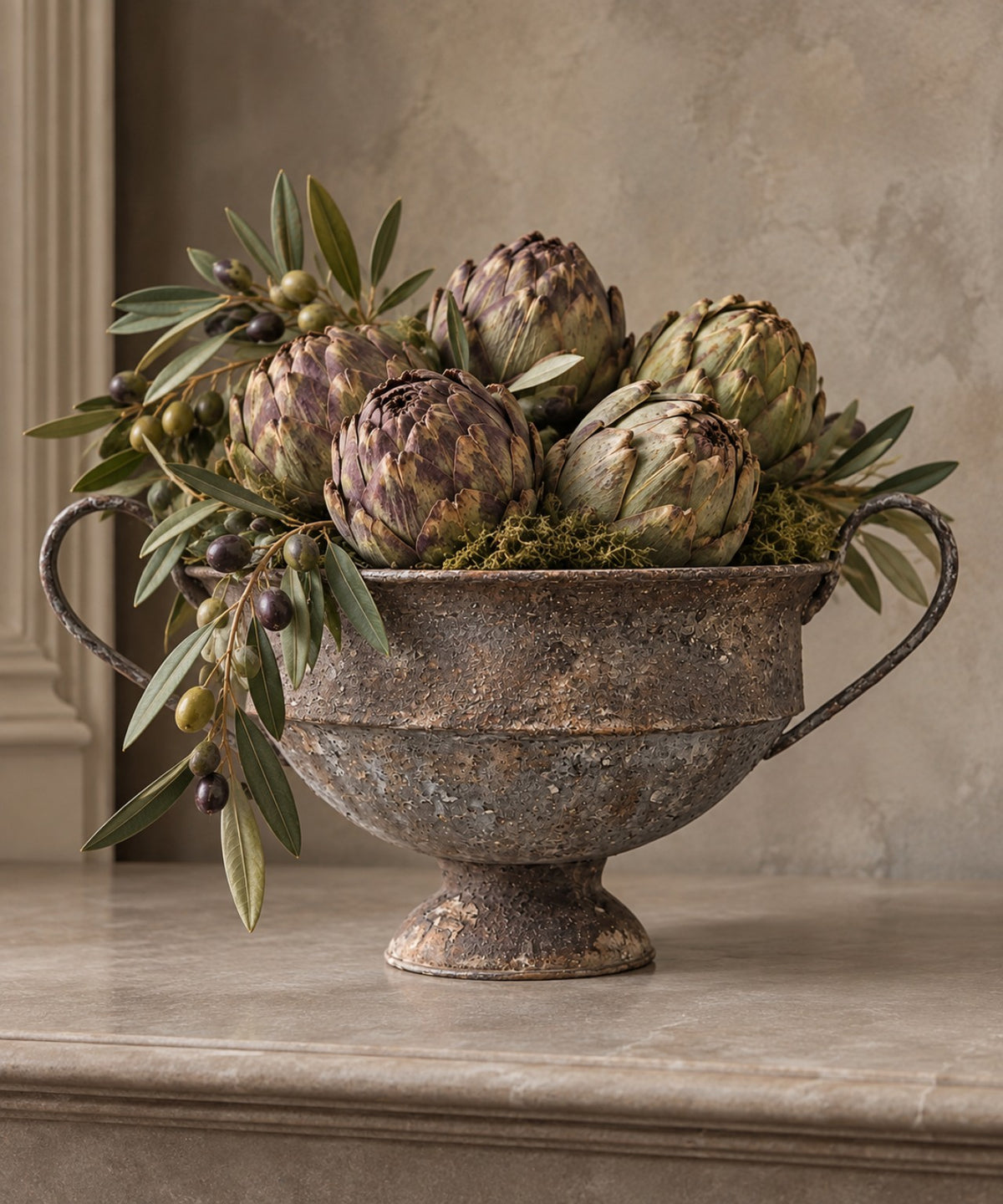 Aubergine metal urn styled with artichokes and olive branches; styling props not included