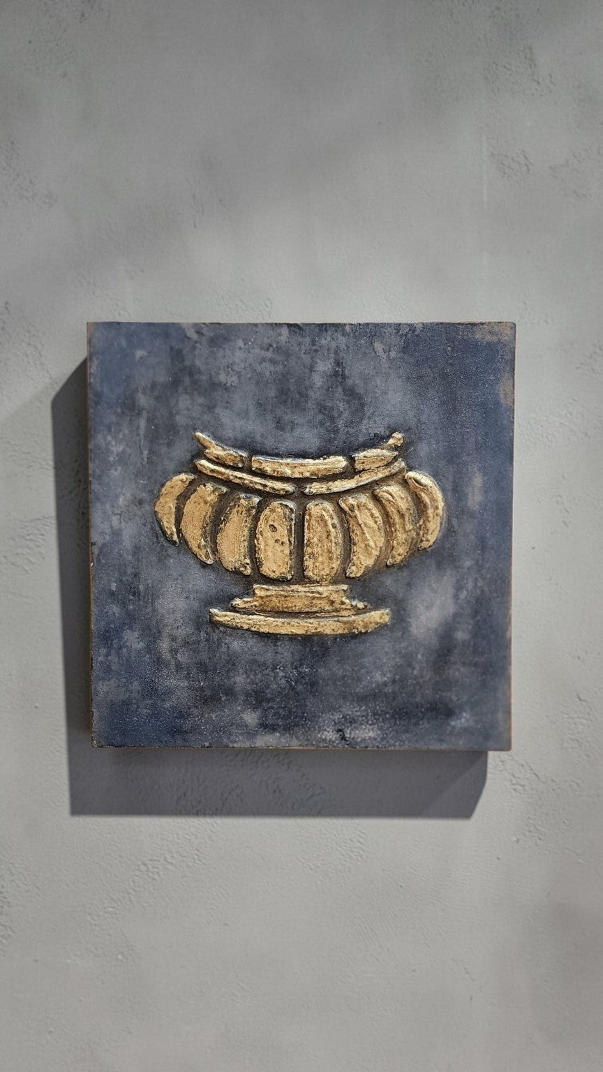 Aged gilded urn wall art shown hanging on a neutral wall
