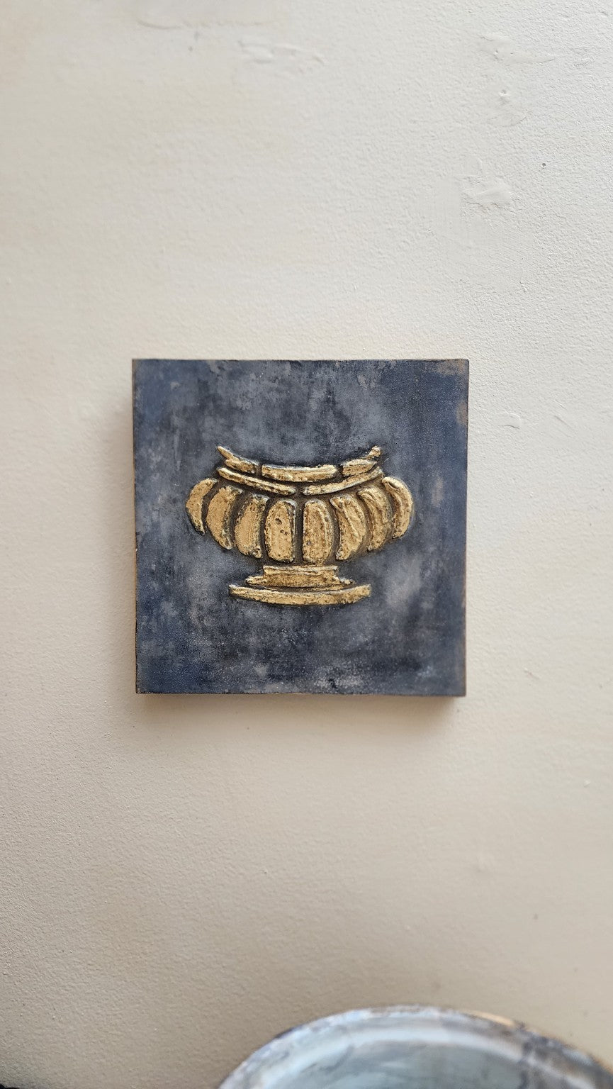 Aged gilded urn wall art displayed on a neutral wall for scale
